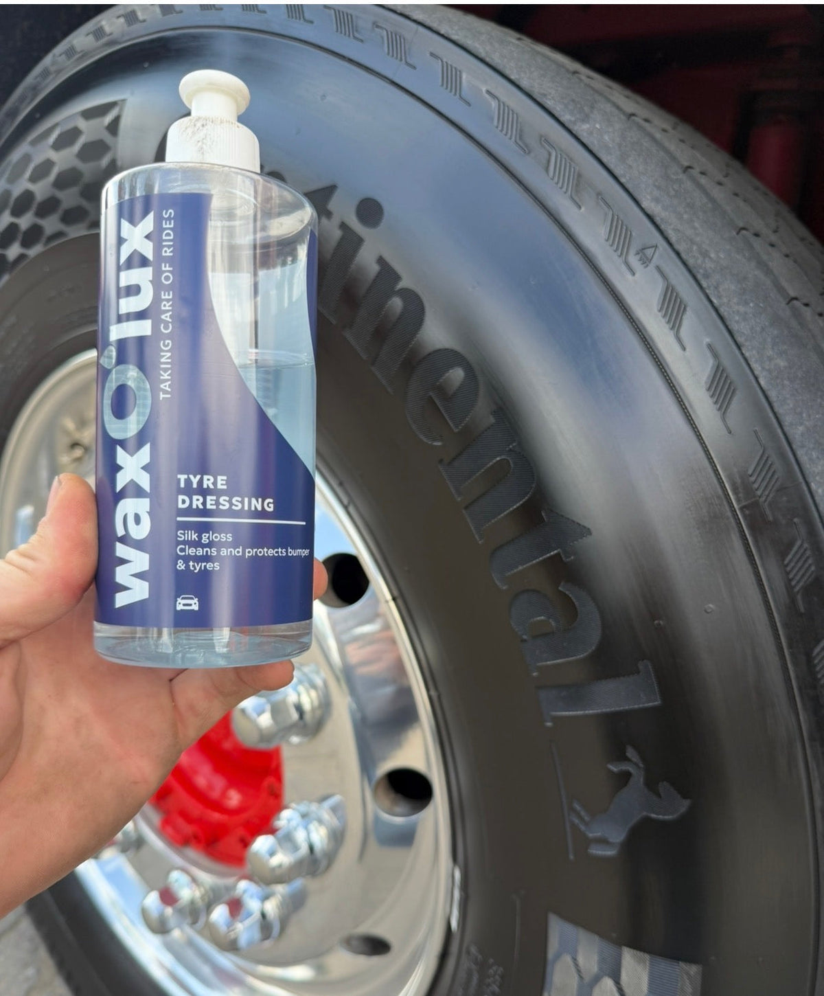Glanzende zwarte autoband met een flesje WaxO'lux Bandenzwart – Tyre Dressing ervoor