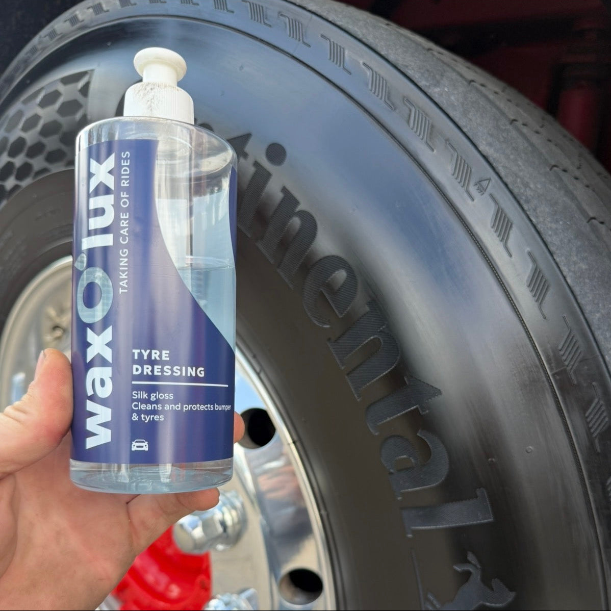 Glanzende zwarte autoband met een flesje WaxO'lux Bandenzwart – Tyre Dressing ervoor
